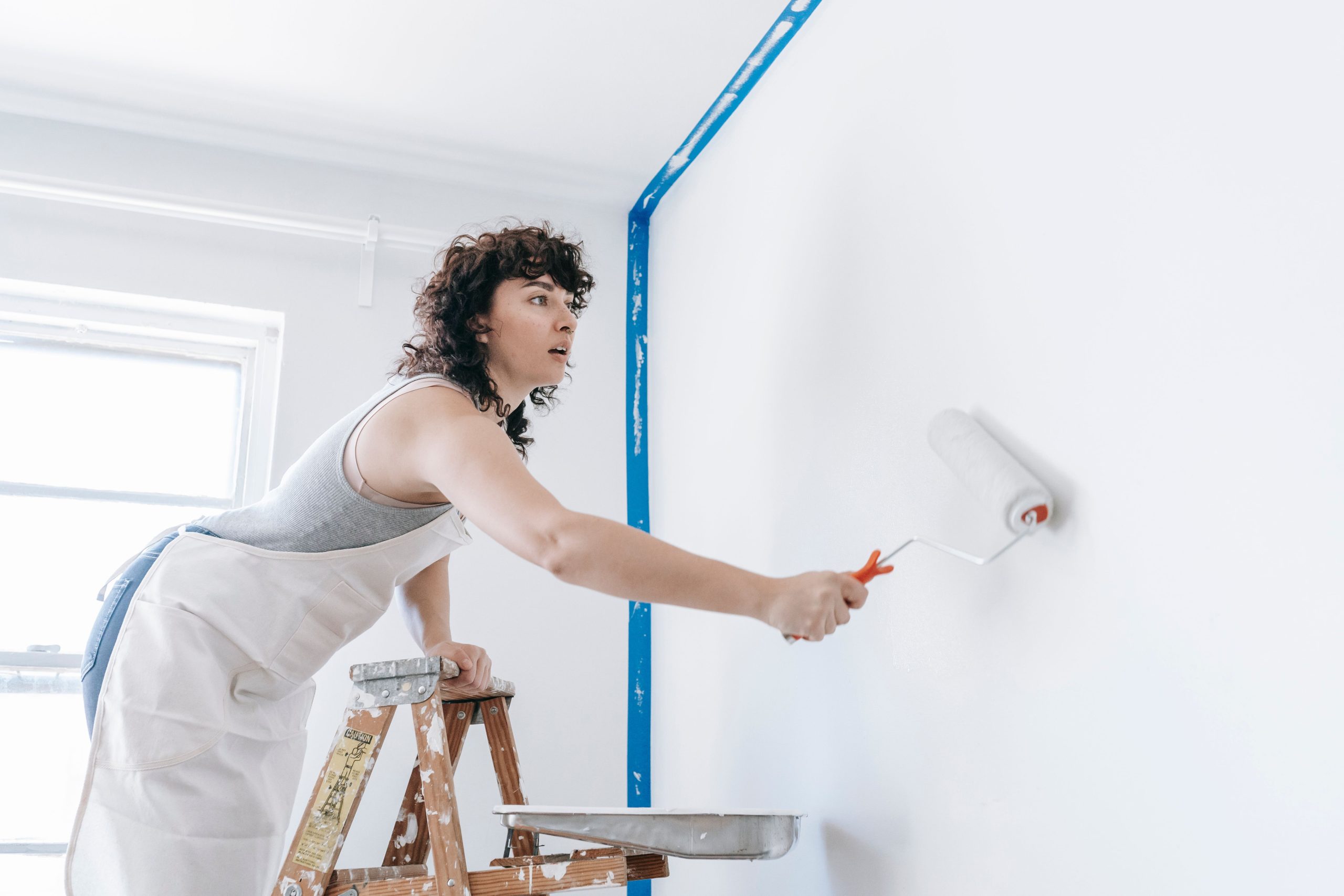 Femme peint mur blanc sur échelle