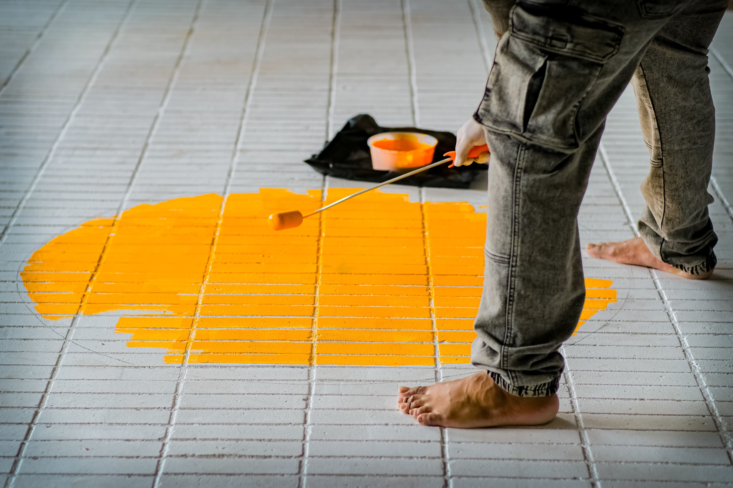 Personne appliquant de la peinture jaune au rouleau sur du carrelage